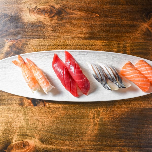 White platter of assorted sushi, including shrimp, tuna, white fish, and salmon, on a rustic wooden table.