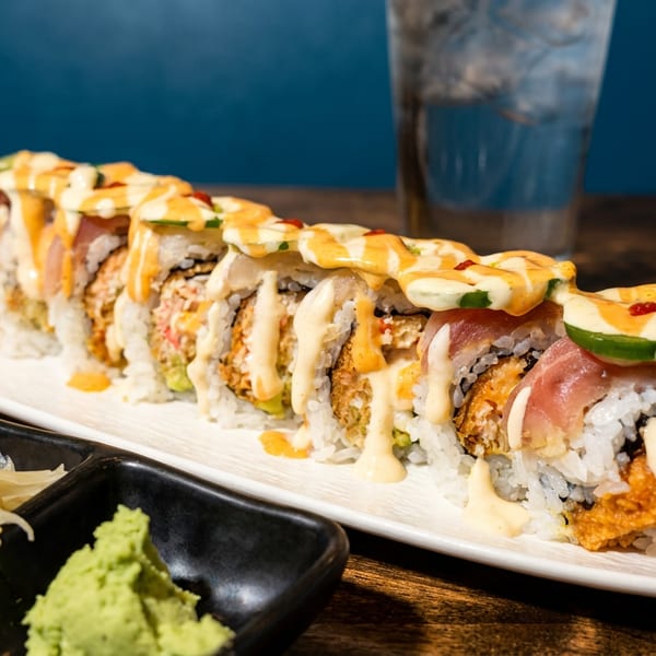 Long sushi roll with various toppings and sauces, served with ginger and wasabi.