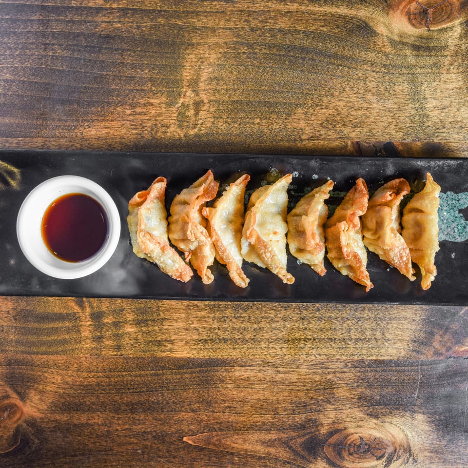 Crispy dumplings arranged on a black platter with dipping sauce on a rustic wooden table.