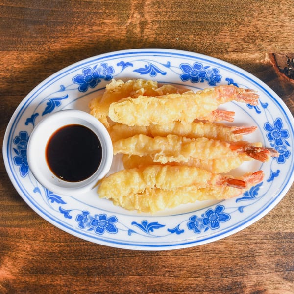 Plate of crispy shrimp and vegetable tempura with dark dipping sauce on a blue-and-white floral dish.