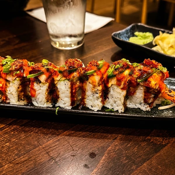 Sushi roll with spicy sauce, green onions, and a shrimp tail, garnished with an orchid.