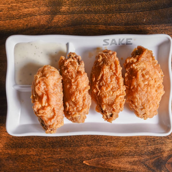 Four crispy fried chicken tenders with creamy dipping sauce on a white divided plate atop a wooden table.