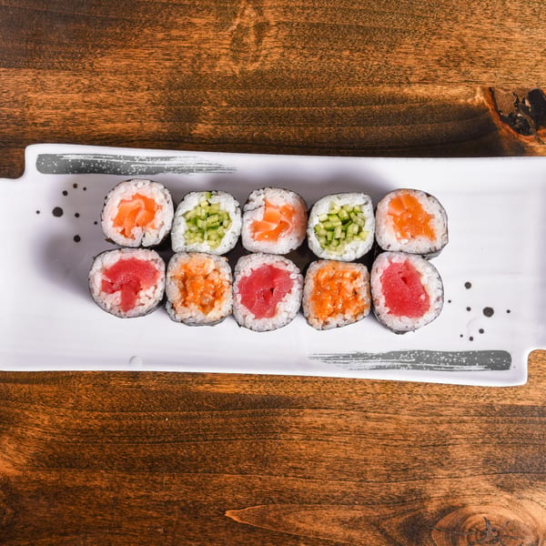 Assorted salmon, tuna, spicy seafood, and cucumber sushi rolls arranged on a white rectangular plate atop a wooden table.